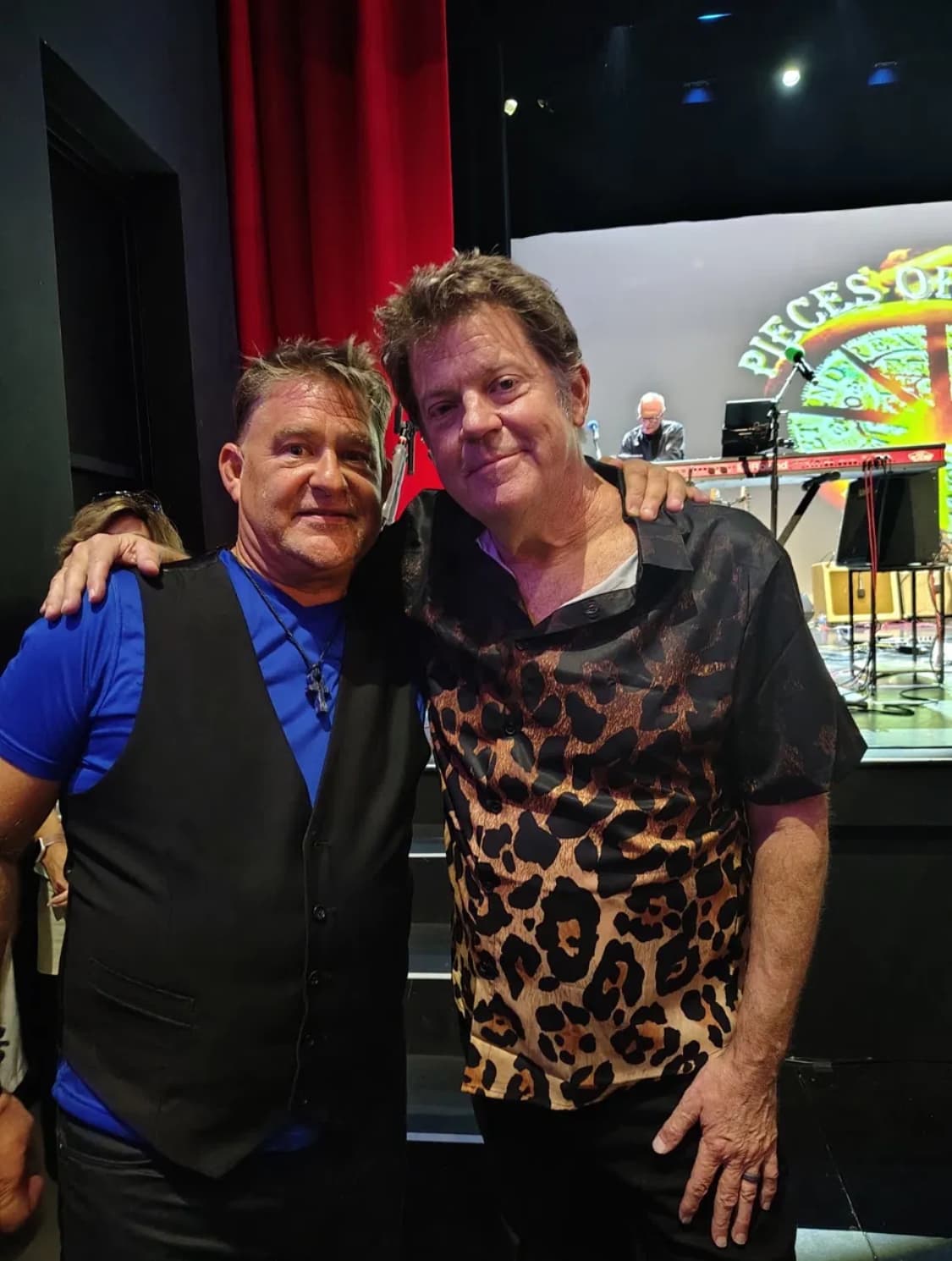 J.C. Grigg and Keith Howland standing together backstage in front of a red curtain and the Pieces of Eight stage
